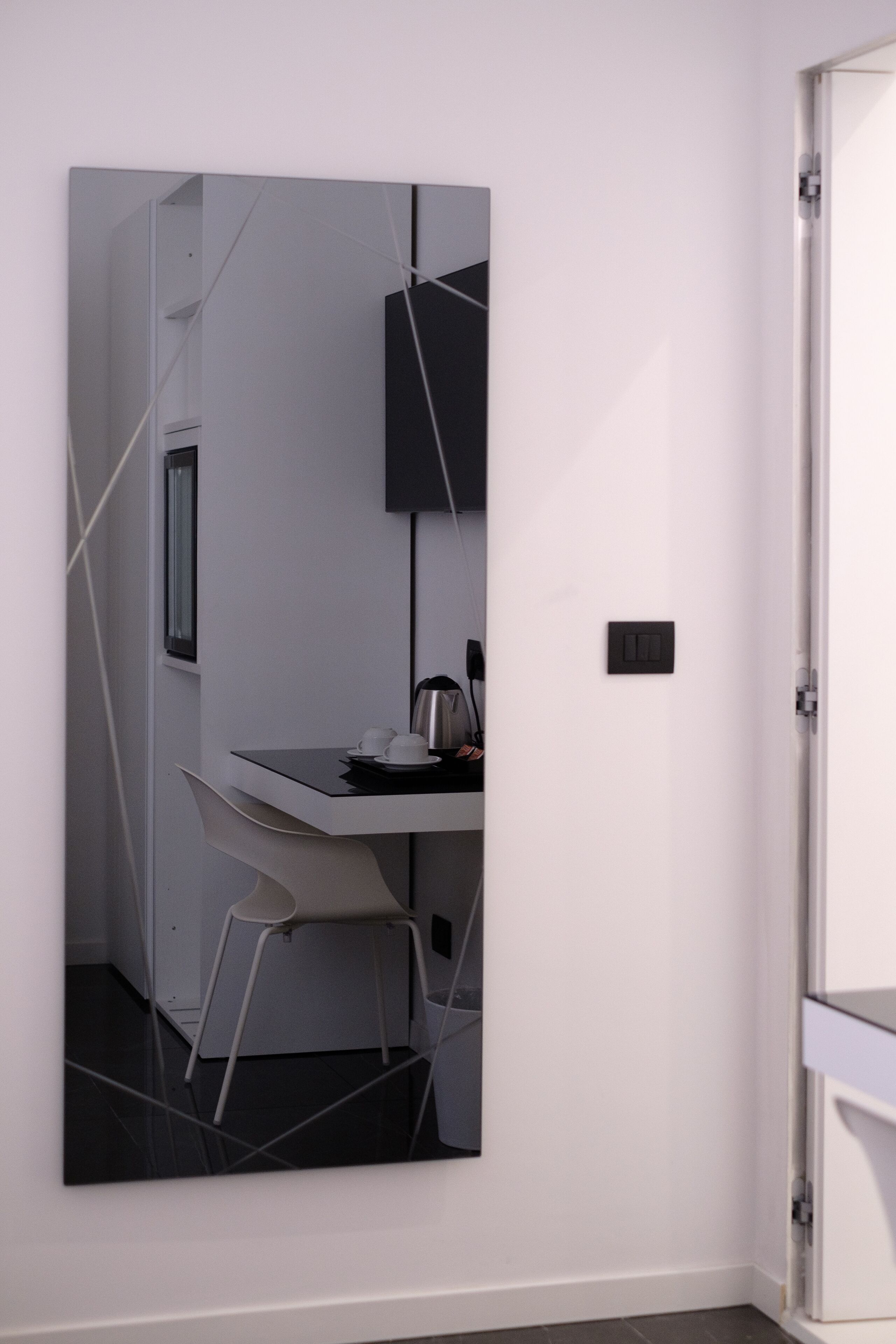 A modern room with a minimalist design, featuring a white wall, a black-framed picture, a white chair, and a small table with a kettle.