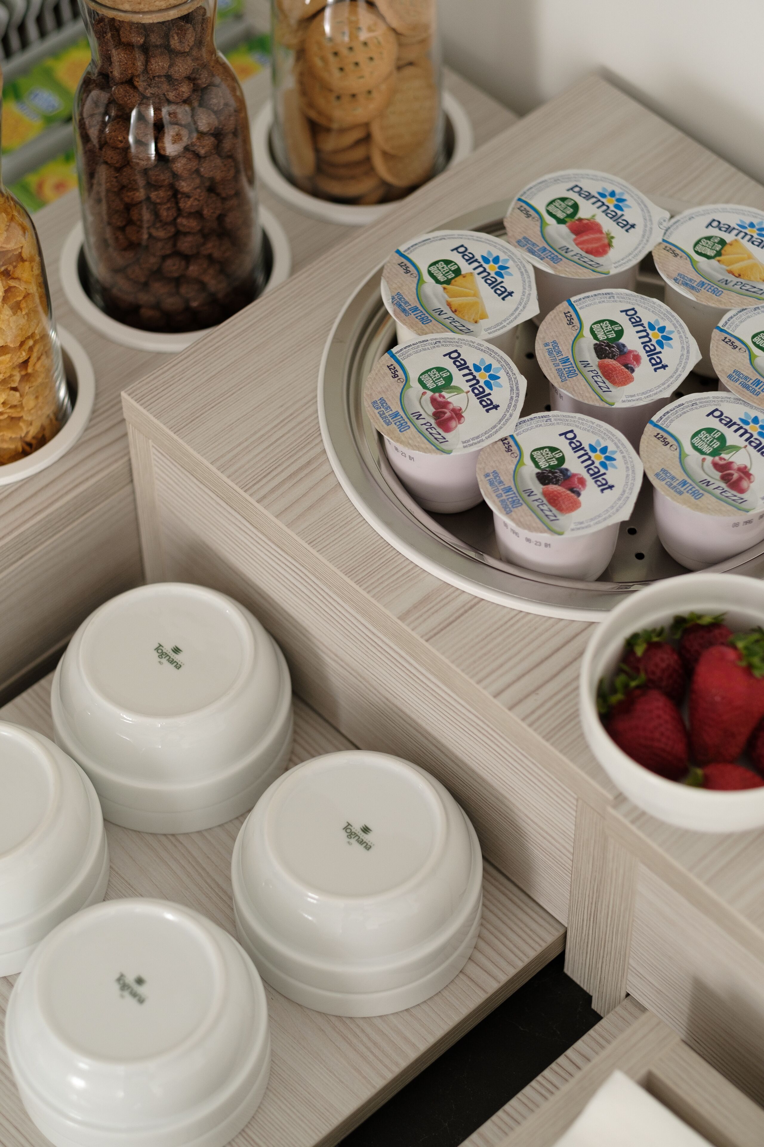 Una bandeja con vasos de yogur y fruta, un tazón de fresas y un tarro de galletas.