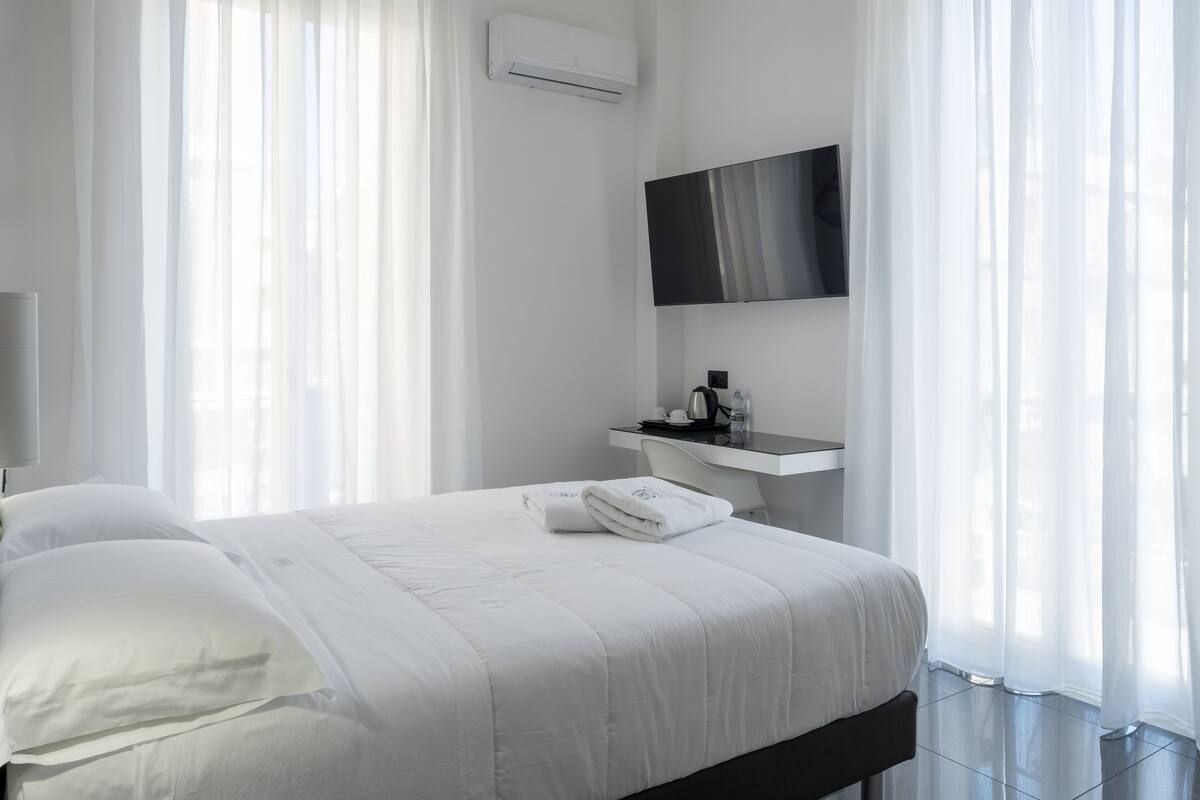 Une chambre d’hôtel moderne avec un lit bien fait, une petite table de chevet avec une bouilloire et un téléviseur fixé au mur.