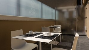 A modern dining area with a glass table, white chairs, and a menu stand. - Domea Superior Rooms (Reggio Calabria)