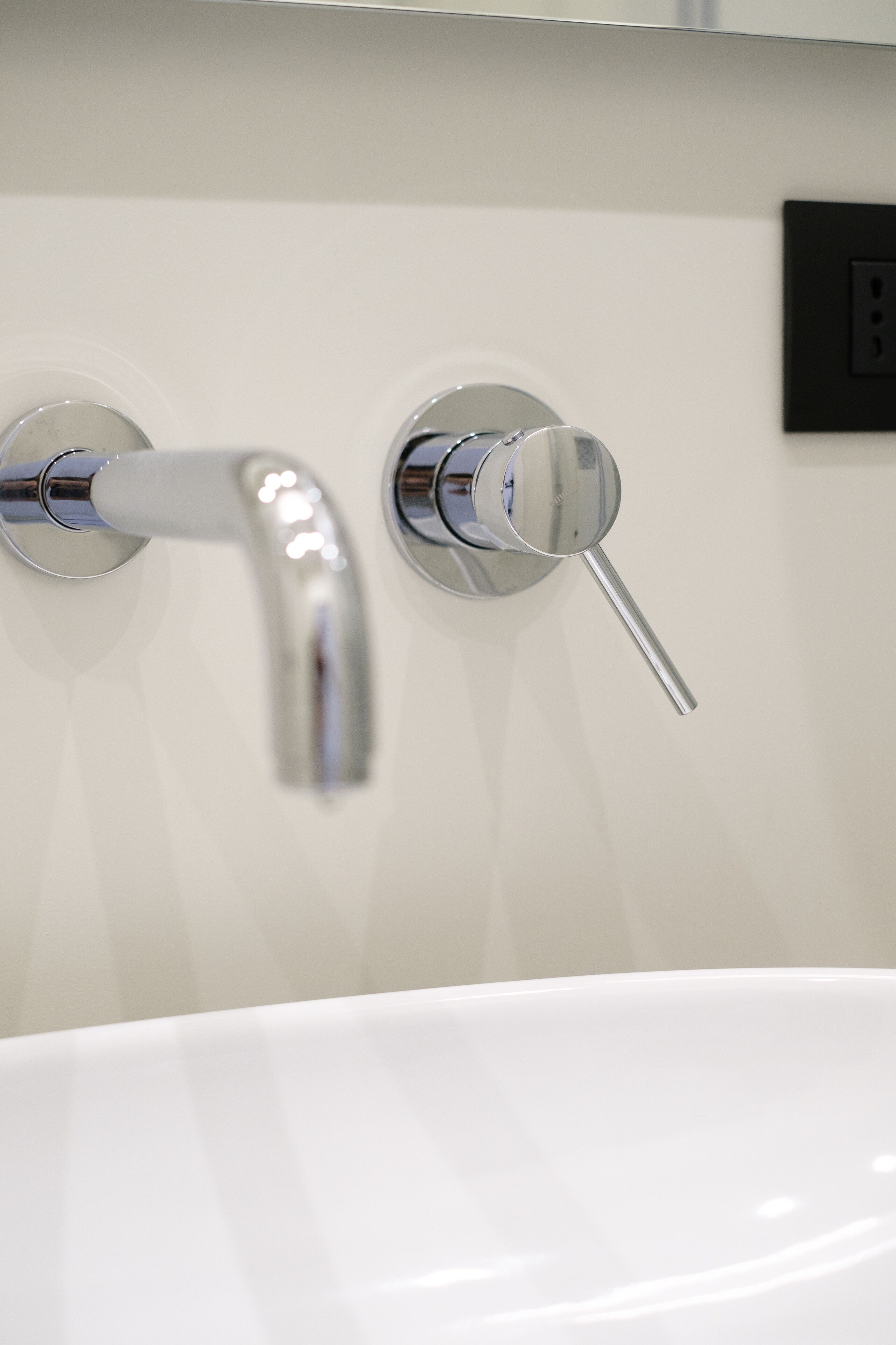 A modern bathroom with a white sink and two chrome faucets.
