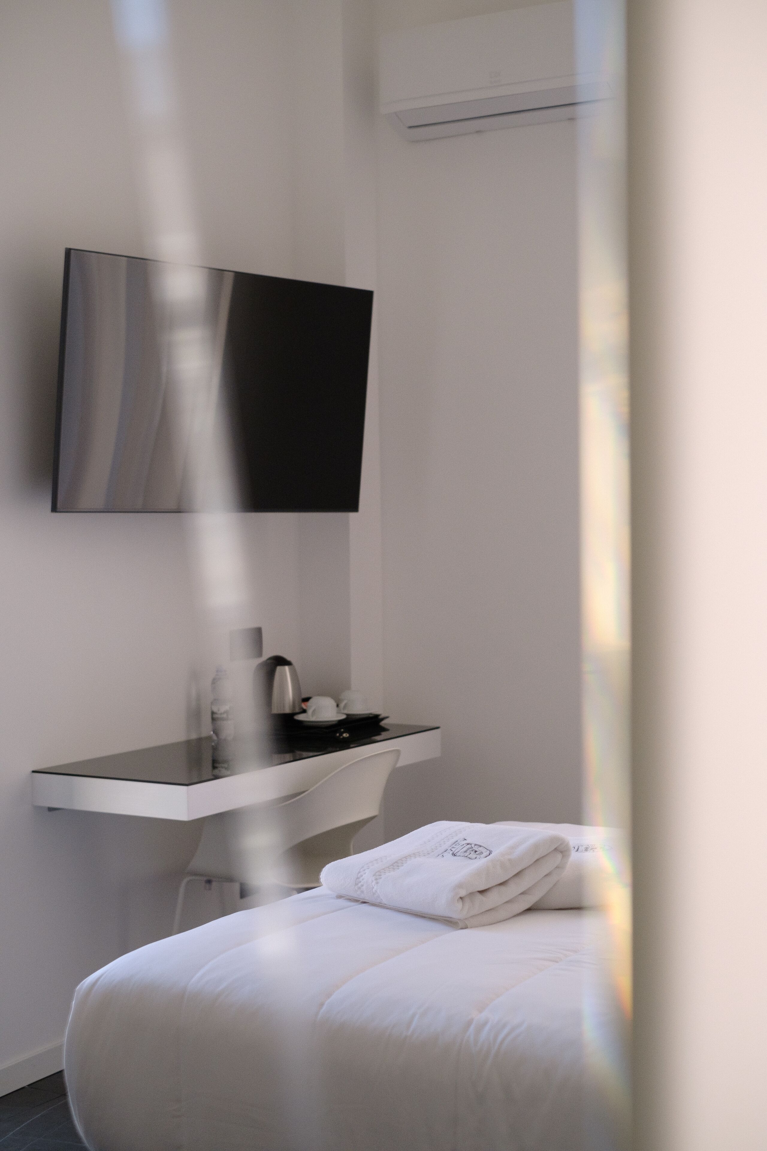Ein modernes Hotelzimmer mit Bett, Nachttisch mit Wasserkocher, flachbildfernseher an der Wand und einer weißen Wand.