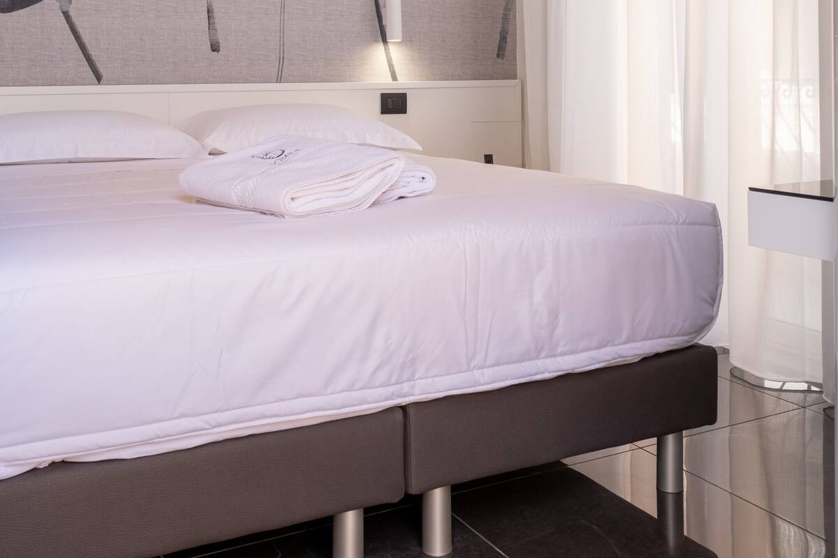 Une chambre d’hôtel moderne avec un grand lit, une lampe fixée au mur et une grande fenêtre avec des rideaux.