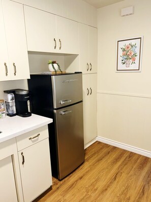 Enjoy cooking in this kitchen with a stainless steel refrigerator, coffee maker, and white cabinetry with gold handles.