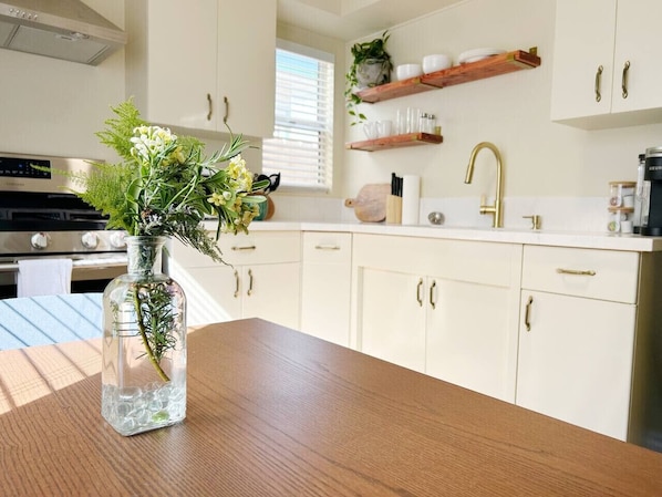 Una cocina con armarios blancos, una mesa de madera y un florero con flores.
