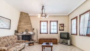 A living room with a sofa, a fireplace, a television, and a herringbone-patterned floor. - Apartment Zina Pelion (Zagora-Mouresi)