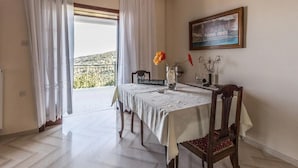 A dining area with a table set for two, a chair, a vase with flowers, and a painting on the wall. - Apartment Zina Pelion (Zagora-Mouresi)