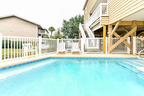 Ein Swimmingpool mit weißem Zaun, einer Holzterrasse und einer Treppe zu einem Balkon.