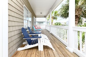 Eine überdachte Veranda mit Holzboden und weißen Geländern, ausgestattet mit mehreren Adirondack-Stühlen und einem Tisch.