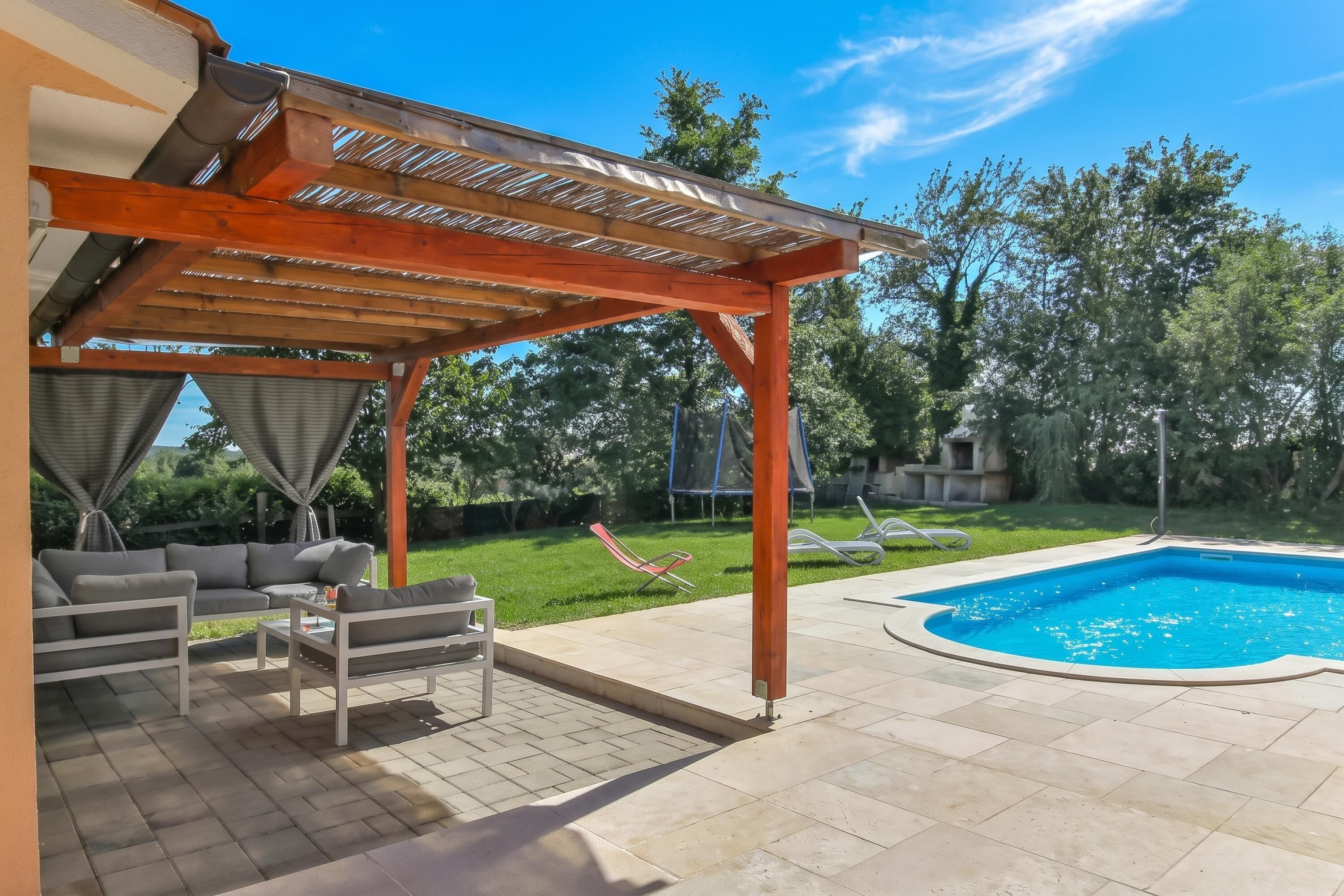 Une terrasse couverte avec des meubles d’extérieur, une piscine et une pelouse.
