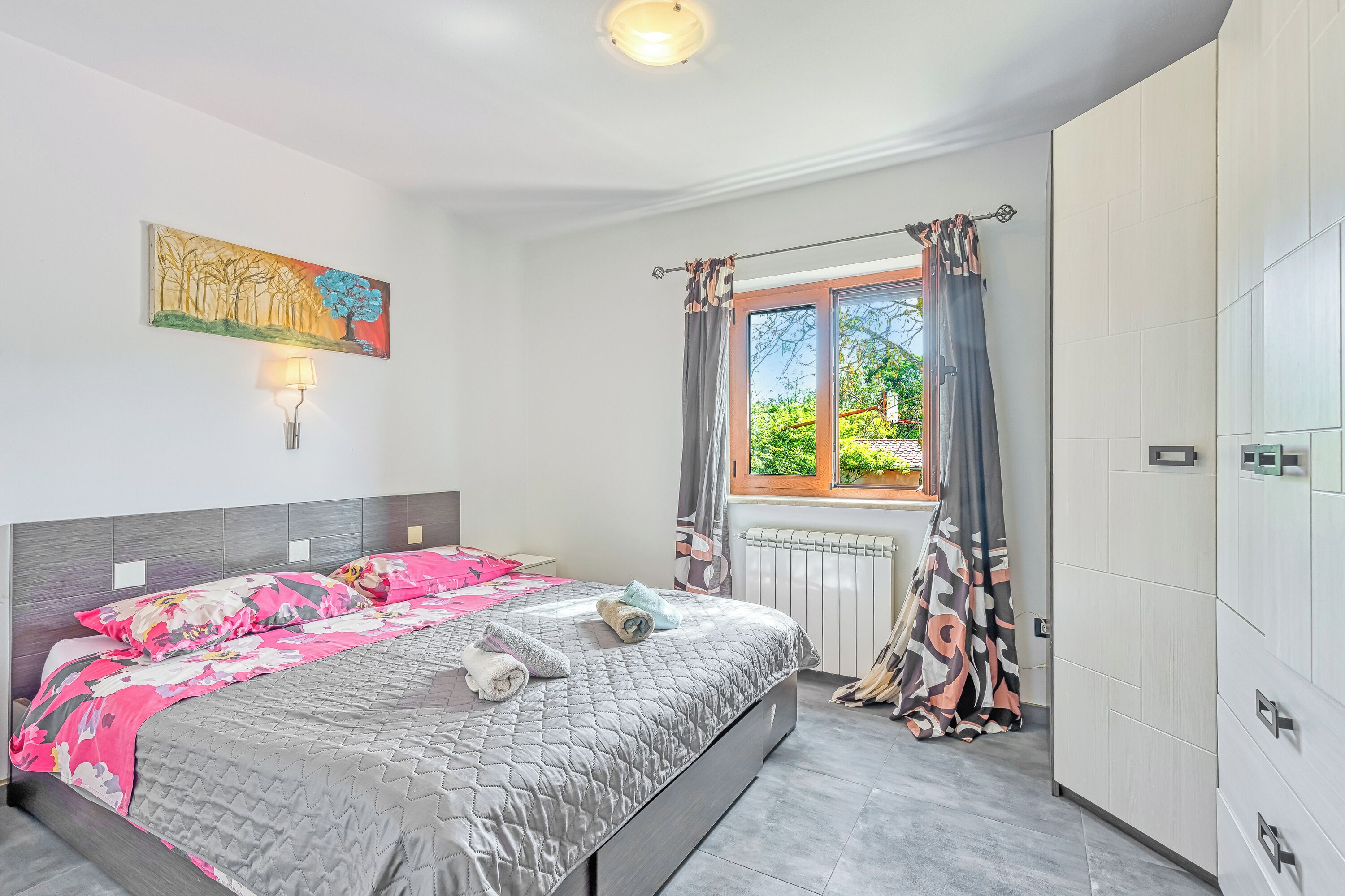 Une chambre à coucher avec un lit, un tableau, une fenêtre avec des rideaux et un radiateur.