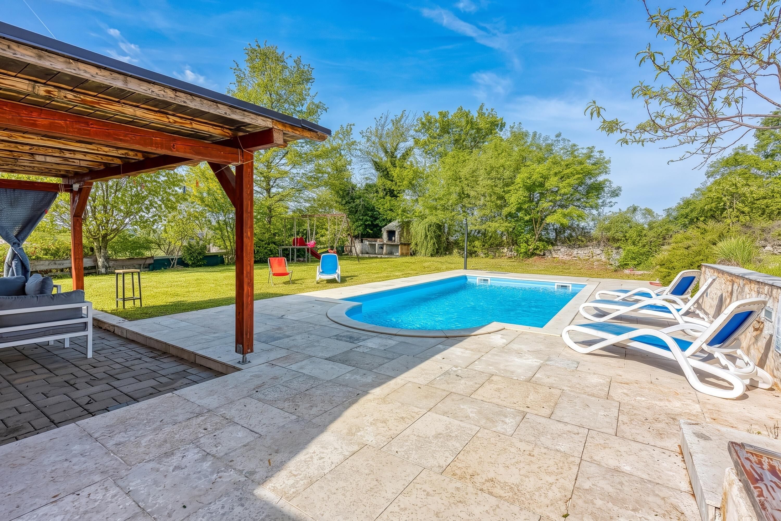 Un jardin avec une piscine, des chaises longues, un espace salon abrité et une pelouse verdoyante.