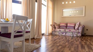 Un coin repas avec une table et des chaises blanches, un canapé à motifs floraux et un plancher en bois.