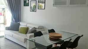 Una sala de estar moderna con una mesa de vidrio, sillas negras, un sofá blanco con cojines y dos cuadros enmarcados en la pared.