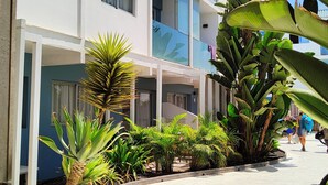 Un hotel de varios pisos con un paseo techado, rodeado de plantas tropicales.