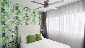Habitación de hotel con cama, ventilador de techo, mesita de noche y pared con estampado de hojas.