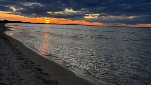 Une plage où l’on peut admirer le coucher de soleil sur l’eau, avec un rivage sablonneux et un ciel nuageux.