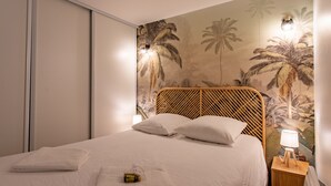 Een net opgemaakt bed met witte lakens en kussens, een houten hoofdbord en een muurschildering van palmbomen.