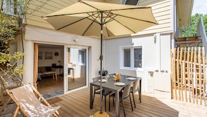 Een terras buiten met een eettafel, een grote parasol en een houten terras.