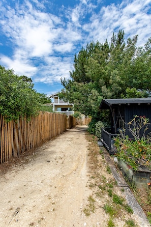 Un chemin de terre mène à une maison bordée d’une clôture en bois d’un côté et d’un abri de l’autre.