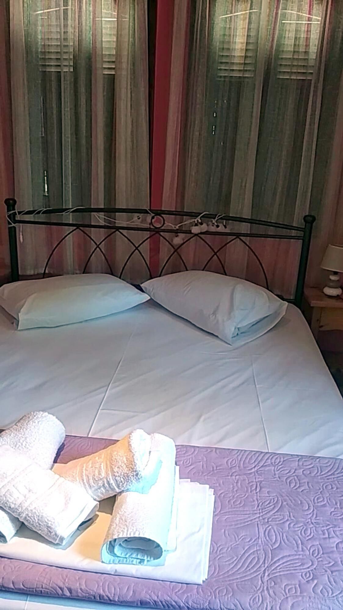 A bed with white linens, a metal headboard, and a purple bedspread.