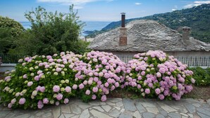 A stone building with a chimney, surrounded by lush greenery and pink hydrangea bushes. - Villa Zina Studio 3 Pelion (Zagora-Mouresi)