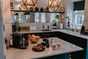 A modern kitchen with a coffee machine, a fruit bowl, and a breakfast setup including pastries and coffee cups. - 37 Jubilee Street (Llandudno)