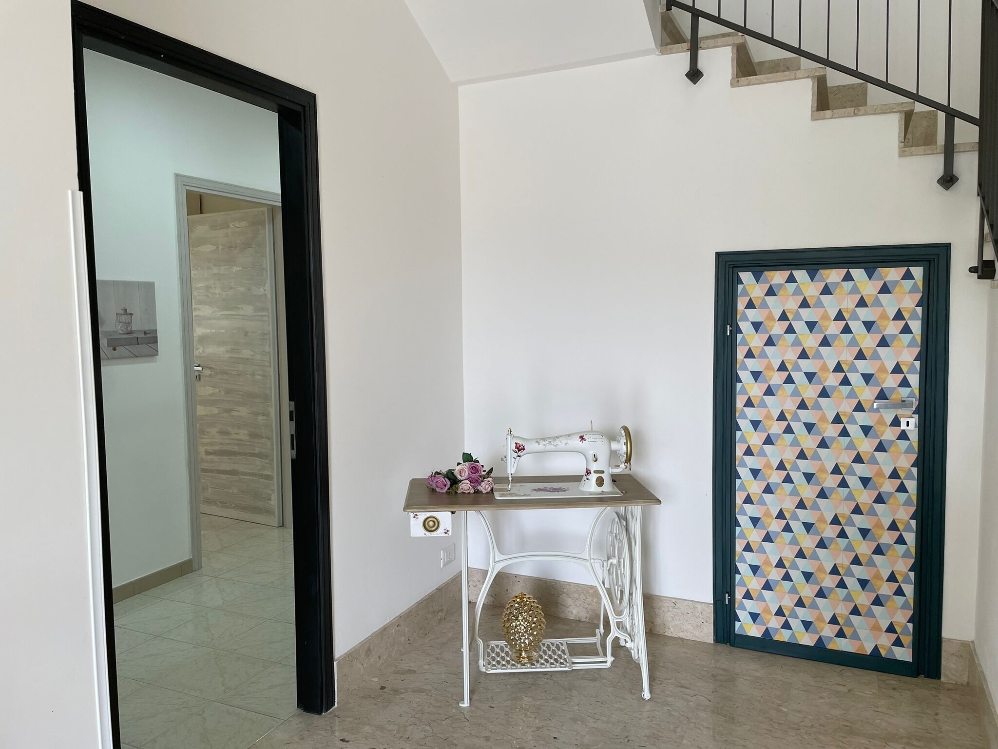 A room with a sewing machine on a table, a patterned door, and a staircase.