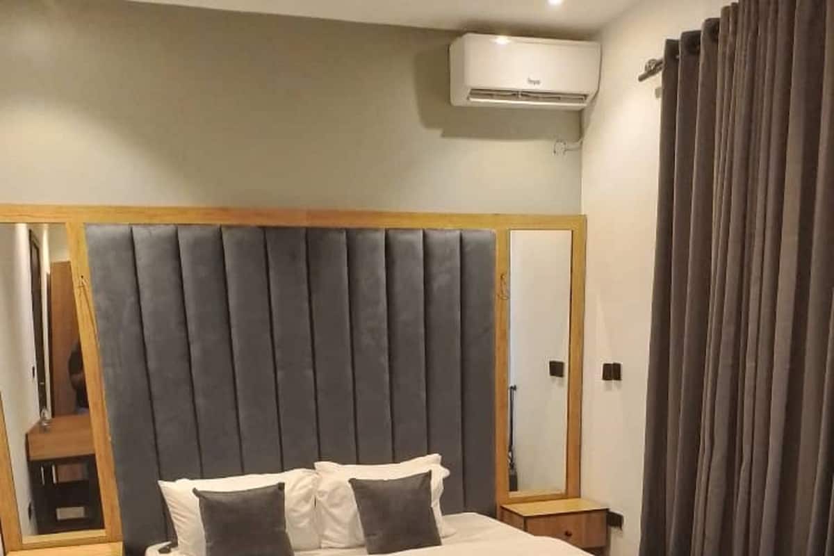 A modern bedroom with a large bed, a wooden nightstand, a mirror, and a window with curtains.