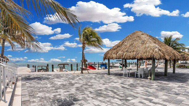 Une terrasse au bord de la plage, agrémentée d’un gazebo à toit de chaume, de palmiers et offrant une vue sur l’océan.