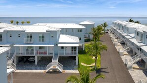 Une rangée de bungalows blancs situés en bord de mer, dotés de balcons, d’un escalier central et offrant une vue dégagée sur l’océan.