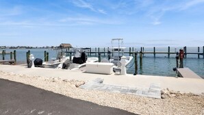 Un port de plaisance avec des bateaux amarrés, une jetée s’avançant dans l’eau et, au fond, une construction au toit de chaume.