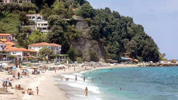 Ein Strand mit Badegästen und Sonnenanbetern, umgeben von Gebäuden und Bäumen.