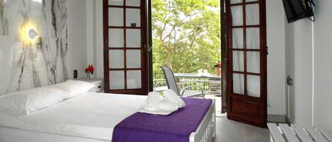 A bedroom with a bed, a purple blanket, a white bench, and a TV on the wall.