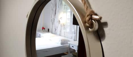 A round mirror with a rope handle, reflecting a bedroom with a bed, bedside table, and a nightstand.