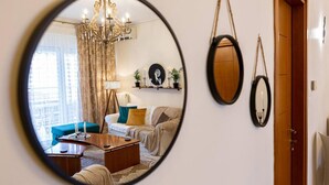 A living room with a round mirror, a chandelier, a sofa, and a coffee table. - Armonia Rentals Volos Flat (Volos)