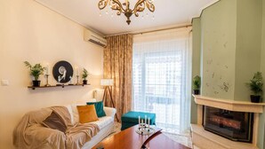 A living room with a sofa, coffee table, and fireplace. There are plants on shelves and a window with curtains. - Armonia Rentals Volos Flat (Volos)