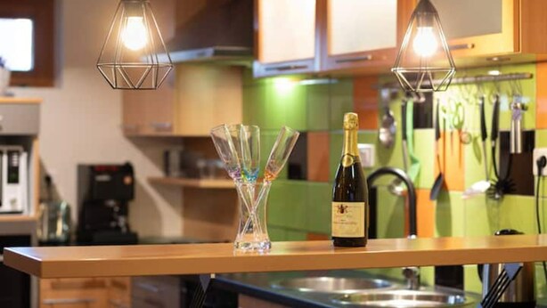 A kitchen counter with a bottle of wine, a glass vase, and hanging pendant lights. - Gîte Classé 3 Avec Sauna Chez Chanchan 4/ 6 Pers (Dambach-la-ville)