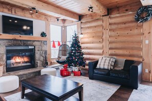 A cozy log cabin interior with a fireplace, a Christmas tree, and a comfortable seating area.