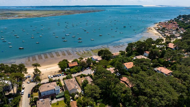 An aerial view of a coastal area with numerous boats, a beach, and residential buildings.