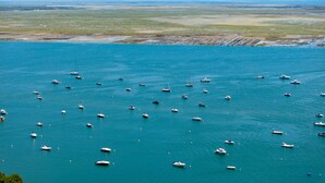 A coastal area with numerous boats anchored in the water, a sandy beach, and a distant shoreline.