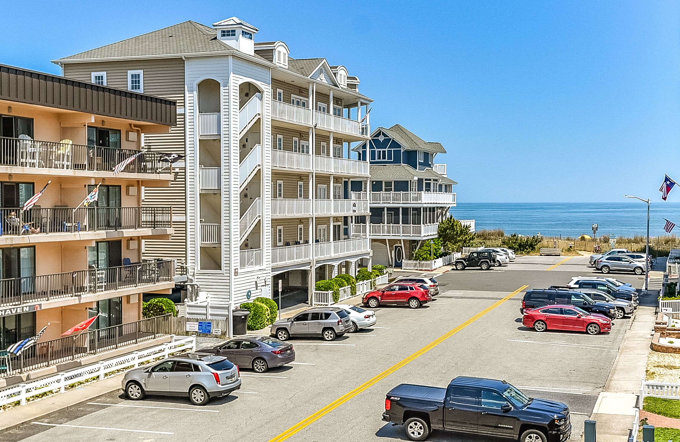 A multi-story hotel with balconies, a parking lot, and a view of the ocean.