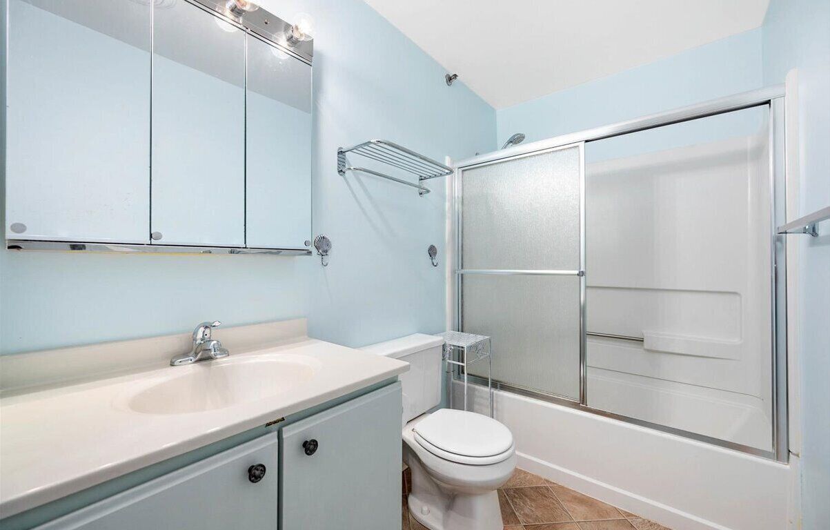 A bathroom with a white sink, a toilet, a glass shower enclosure, and a mirror with lights.