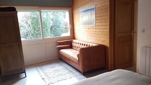 A room with a wooden wall, a window, a brown sofa, a patterned rug, and a radiator. - Maisonnette (Chambéry)