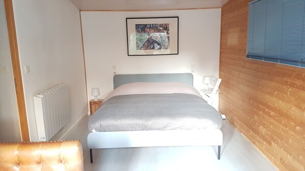 A bedroom with a bed, a bedside table with a lamp, a radiator, and a framed picture on the wall.