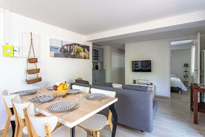 Un salon moderne avec un coin repas, un canapé gris, un téléviseur à écran plat et une vue sur la mer par la fenêtre.