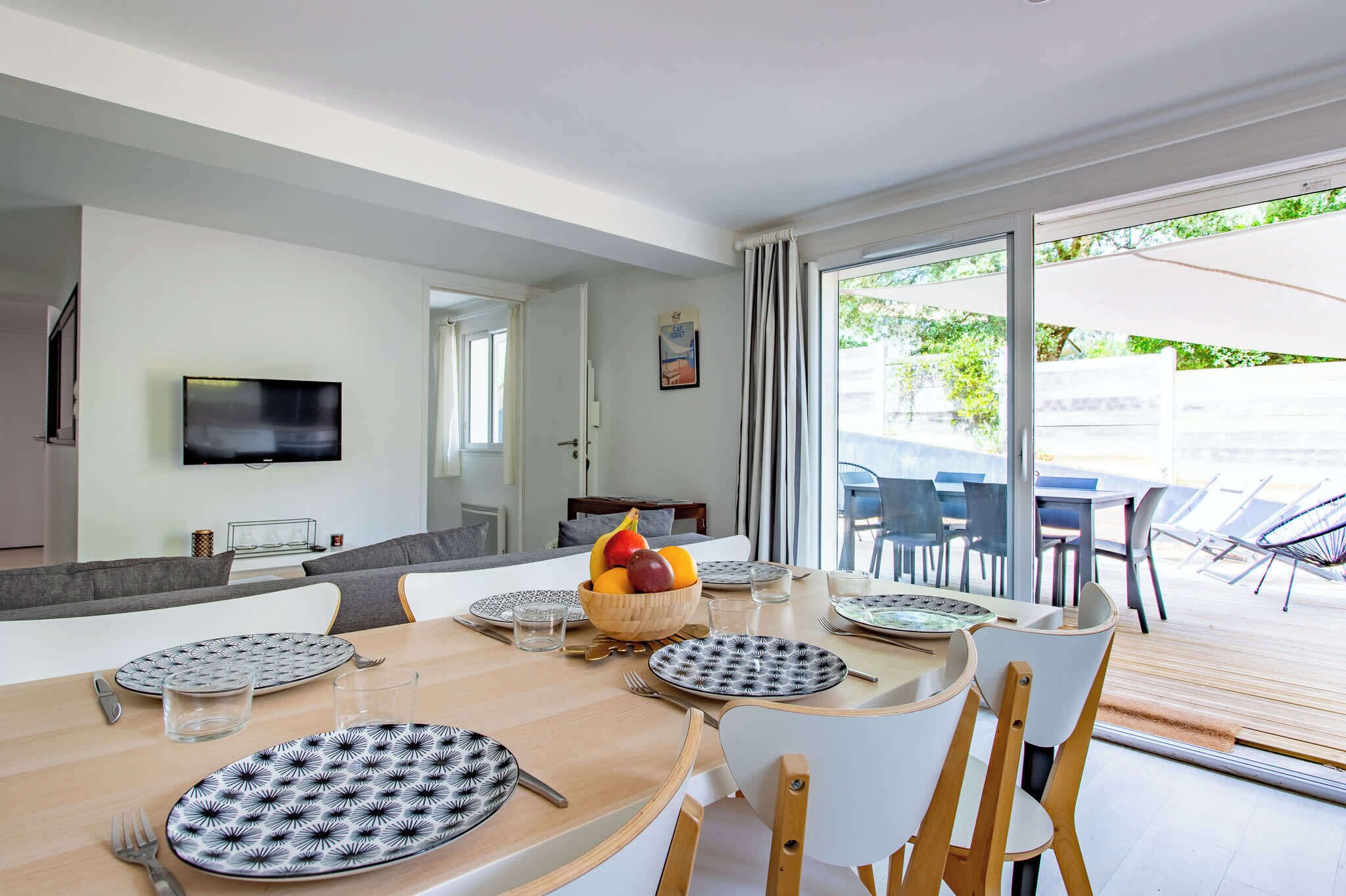 A dining area with a table set for four, a fruit bowl, and a television on the wall.