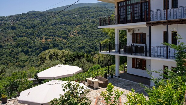 A two-story building with a balcony, outdoor seating, and a view of a mountainous landscape. - Paradeisos Double Room With Sea View 4 (Zagora-Mouresi)