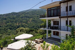 A two-story building with a balcony, outdoor seating, and a view of a mountainous landscape.