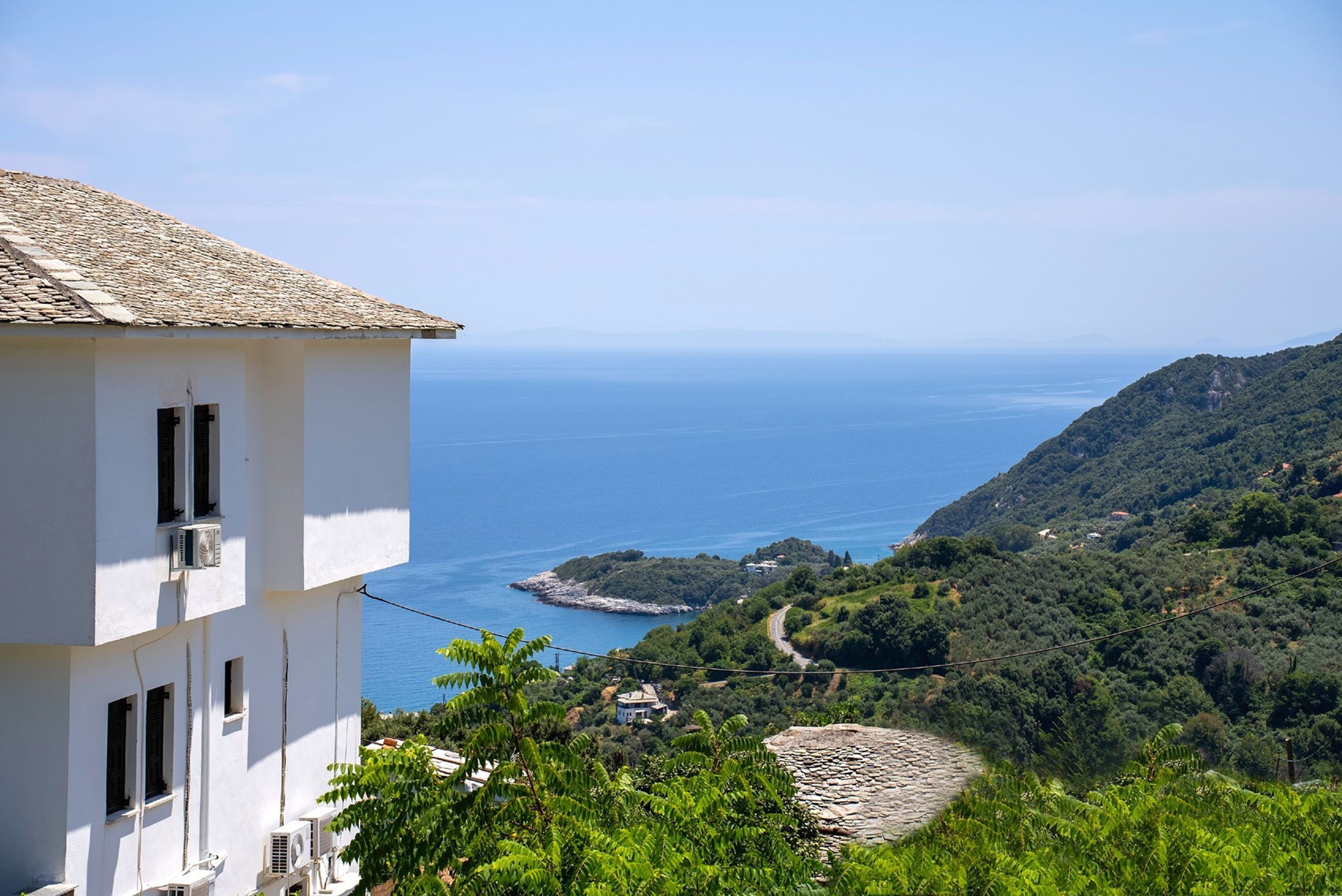 A white building with air conditioning units, overlooking a coastal landscape with a clear view of the sea and a hilly terrain.